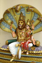 Colurful statue of a lion headed God with four arms and a female figure sitting on his lap at an Indian Hindu Temple