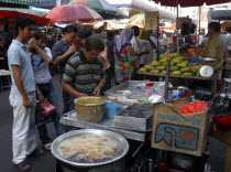 Market stalls selling various foodstuffs with customers waiting for hot food in the foreground