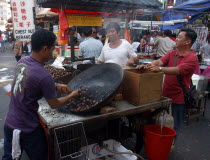 Market stall selling hot snacks cooked in a large wok with vendor and customers