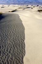 View along the ridge of a sand dune in the desert landscape with a rocky hills in the distance