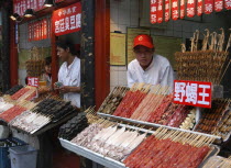 Kebab stall displaying assorted skewered meat with vendor standing behind
