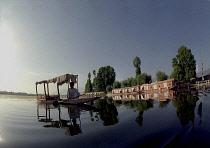 Nagin Lake. Man in Shikara or Water Taxi with two modern houseboats moored at the edge of the lake