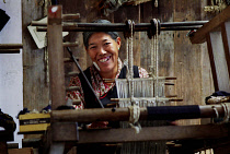 Smiling Tibetan lady weaving fabric on a loom