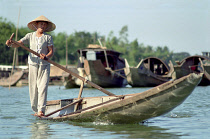 Local transport woman standing on the edge of her canoe rowing with a single oar.