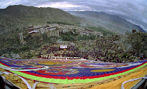 Wide angled view looking down massive colourful image of buddha to Parade toward the Thangka with onlookers at a silken Thangka Buddhist ceremony for the cycle of life