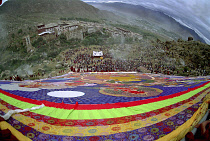 Wide angled view looking down massive colourful image of buddha to Parade toward the Thangka with onlookers at a silken Thangka Buddhist ceremony for the cycle of life