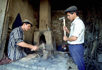 Blacksmith beating heated metal in his workshop with helper