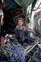 Young hardware vendor sitting amongst goods for sale