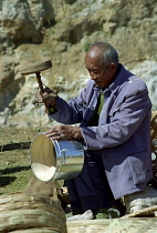 Man using old style drilling tool on metal and wooden pot