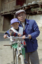 Portrait of a man standing with a small boy on his bike holding a Pepsi bottle