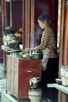 Female vendor at a street stall cooking and serving tea