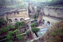 View over cave dwellings built into the cliffside with man tending to gardens outside