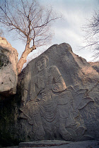 Angled view of seated Buddha rock carving in cliff face