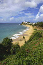 View from green cliffs over empty golden sandy stretch of beach