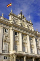 Angled view looking up at the Palacio Real facade with the Spanish flag flying from the rooftop