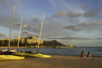 Diamond Head. Sandy beach with two people sitting near boats on the sand in evening light