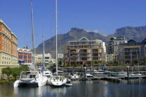 View of the waterfront with moored boats and buildings against a backdrop of mountains