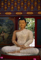 Wat Chayamangkalaram.  Interior with seated Buddha figure in meditative pose framed by red window frame.  Wall painting depicting religious scene at side.