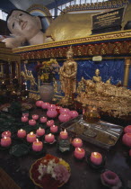 Wat Chayamangkalaram.  Interior.  Part view of  reclining Buddha lying behind smaller figures covered in gold leaf and lighted candles in the shape of lotus flowers. Also known as Wat Buppharam.