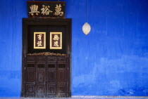 Cheong Fatt Tze Mansion.  Restored Chinese merchants house.  Wooden doorway with gold Chinese letters set into blue painted wall with lantern hanging at side.