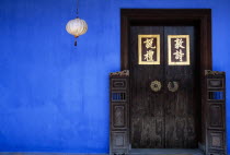 Cheong Fatt Tze Mansion.  Restored Chinese merchants house.  Wooden doorway with gold Chinese letters set into blue painted wall with lantern hanging at side.