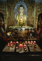 Dharmikarama Burmese Temple.  Interior with pink lotus flower shaped lighted candles in front of large seated Buddha and small golden Buddha figures.