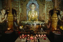 Dharmikarama Burmese Temple.  Interior with pink lotus flower shaped lighted candles in front of large seated Buddha and small golden Buddha figures.