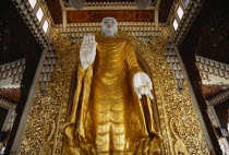 Dharmikarama Burmese Temple.  Interior with large standing Buddha figure with raised hand in gold painted robe and ornate carved gold panel behind.