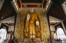 Dharmikarama Burmese Temple.  Interior with large standing Buddha figure with raised hand in gold painted robe and ornate carved gold panel behind.