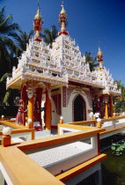 Dharmikarama Burmese Temple.  Exterior with ornate carved roof and statues.  Visitors outside arched entrance.