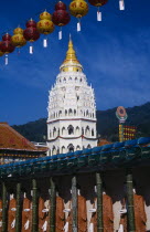 Covered colonnade with line of standing Buddha figures and Ban Po  the Pagoda of a Thousand Buddhas behind.  String of red and yellow Chinese lanterns above.