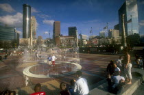 Centennial Olympic Park.  Visitors around paved area with fountains  city skyline behind.