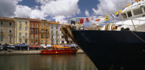 Sete.  Part view of harbour and colourful waterside buildings with prow of boat draped with flags in the foreground.
