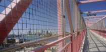 Williamsburg Bridge.  View along footbridge lined by high sided metal barriers towards city skyline.