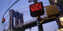 Part view of Brooklyn Bridge at dusk with traffic lights displaying Dont Walk sign in the foreground.
