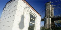 Part view of Brooklyn Bridge with shadow cast by street lamp on exterior wall of white painted building in the foreground.