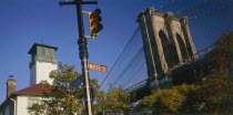 Part view of Brooklyn Bridge seen above trees with road sign and traffic lights in the foreground.