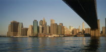 Lower Manhattan.  Post September 11 skyline from Brooklyn in warm  golden light with underside of bridge in the foreground.