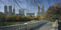 Central Park  Bow Bridge.  View over cast iron bridge across lake lined by trees in autumn colours  overlooked by city buildings and the San Remo towers.
