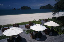 Tourists sitting under umbrellas set on decking at the garden restaurant of the Radisson Resort hotel on Pantai Rhu beach Asian Beaches Malaysian Sand Sandy Seaside Shore Southeast Asia Tourism Holid...