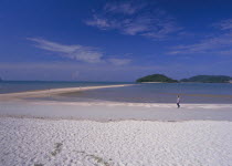 Pantai Cenang beach with man walking near the the sand bar at low tide to Pulau Rebak Kecil island