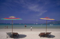 Empty deckchairs and parasols on the beach with people walking by the water