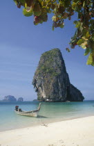 Long tail boat in clear calm blue water at the edge of he beach with limestone islands behind