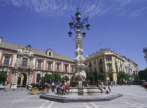 Santa Cruz District  Plaza Virgen de los Reyes with Palacio Arzobispal on the left and a horse carriage passing a fountain with people sitting down