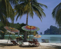 Beach in enclosed bay with deckchairs and umbrellas beneath coconut palm trees