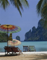 Beach in enclosed bay with deckchairs and umbrellas beneath coconut palm trees