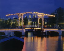 Magere Brug the Skinny Bridge illuminated at night with a blue sky and houses in the  background