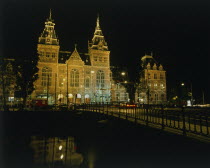 Rijksmuseum illuminated at night beyond a bridge over a canal reflected in the water