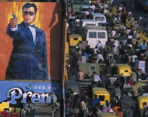 Crowded street of Chandni Chowk with trucks  trishaws and people by cinema hoarding of man pointing a pistol