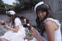 Harajuku District. Two teenage girls sitting together with one eating and the other using a mobile phone
